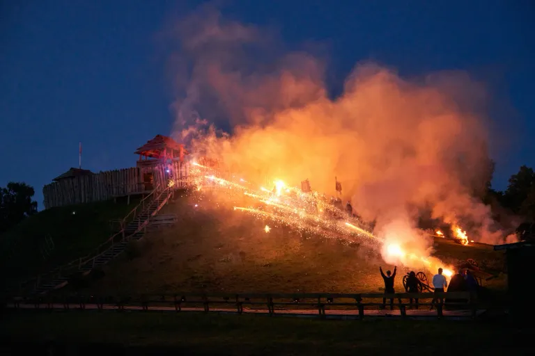 Strumienie iskier i dym nad grodziskiem z drewnianą twierdzą podczas nocnej imprezy masowej