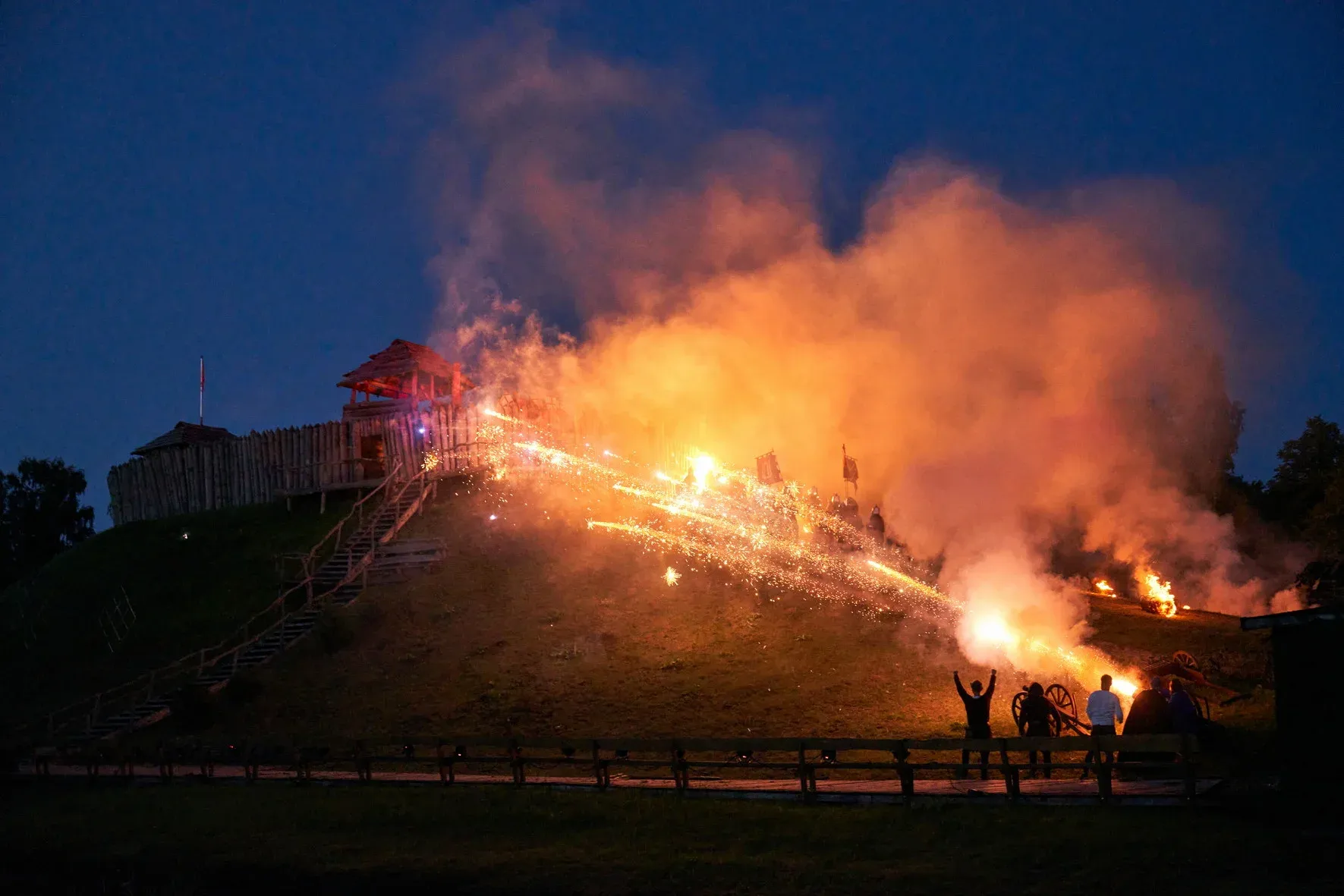 Strumienie iskier i dym nad grodziskiem z drewnianą twierdzą podczas nocnej imprezy masowej