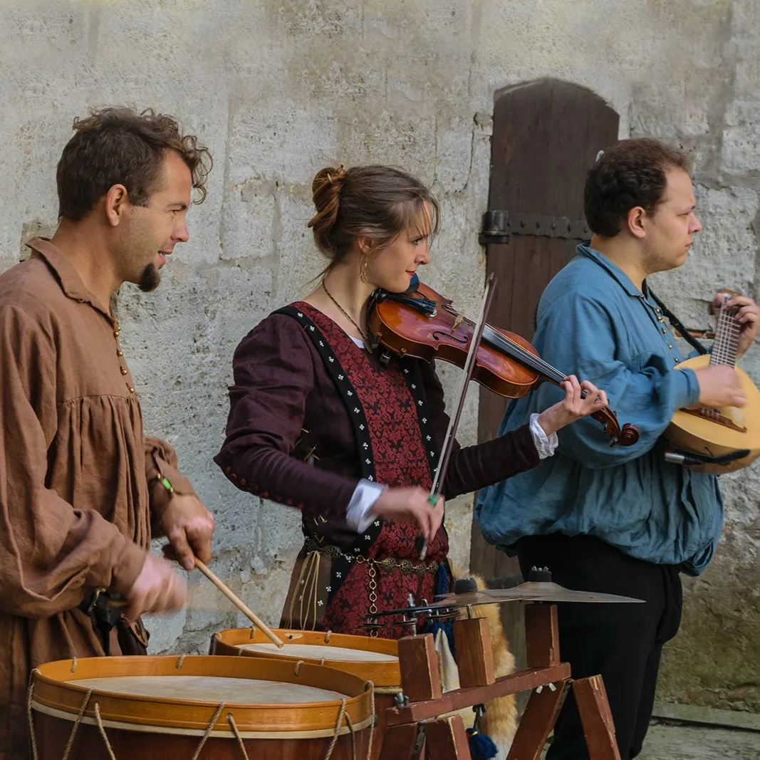 Musicians play drums, violin and lute beside a stone wall