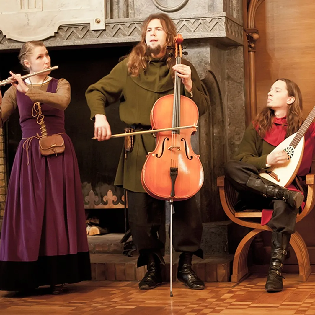 Three musicians play cello, flute and lute beside a fireplace