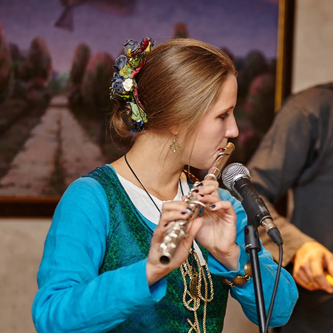 A musician in period dress plays the flute into a microphone