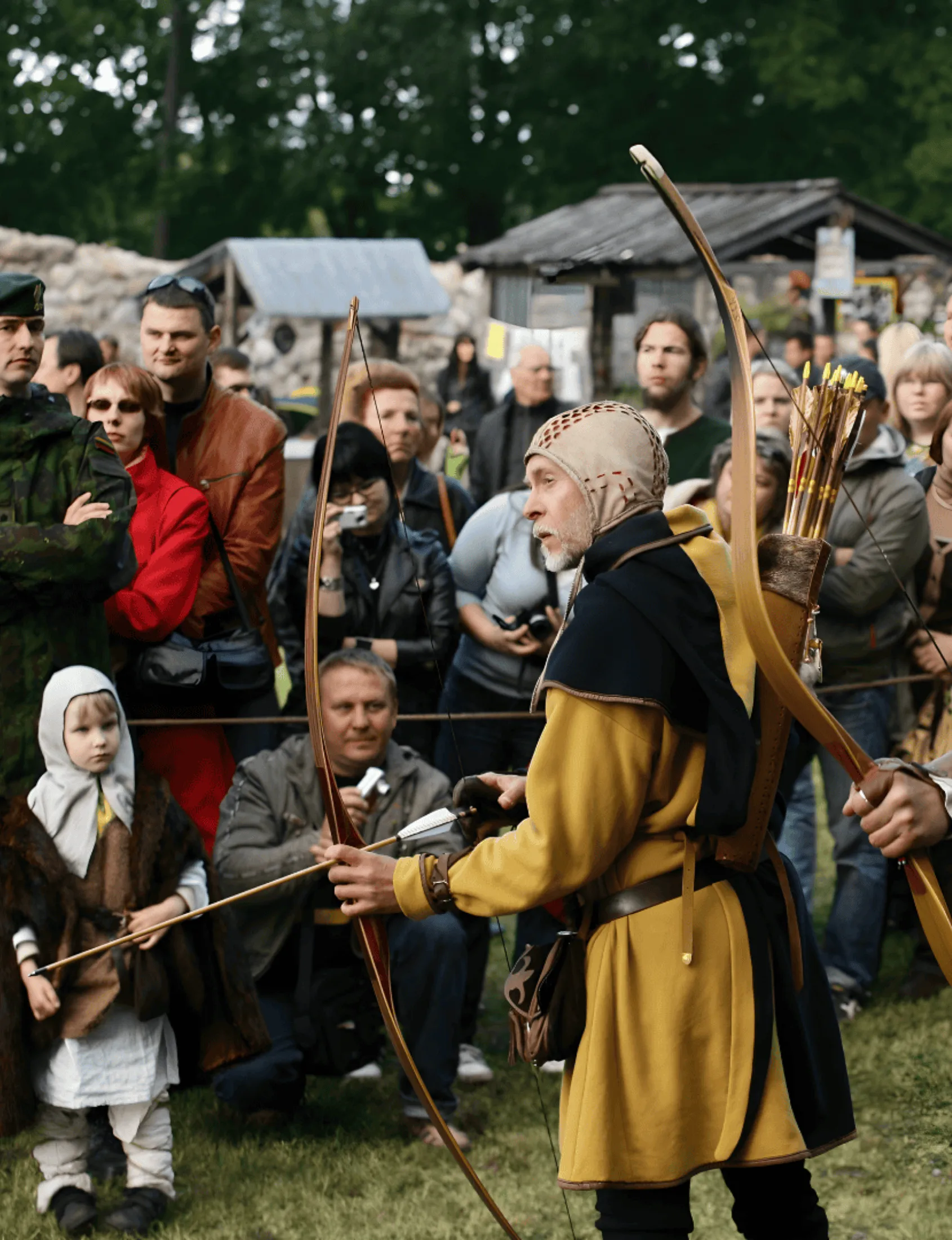An archer in medieval costume draws a bow in front of onlookers