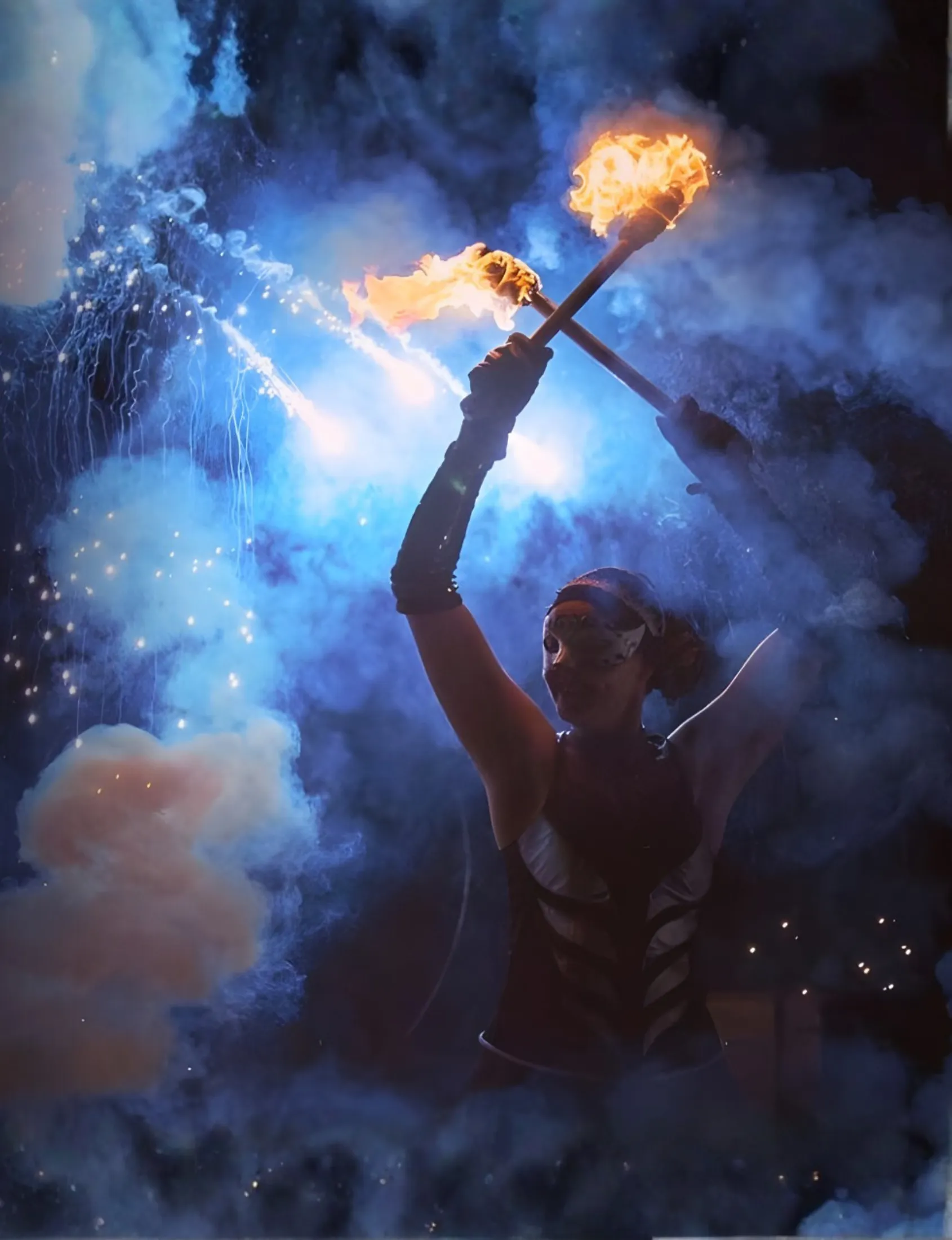 A performer raises two burning torches through blue smoke