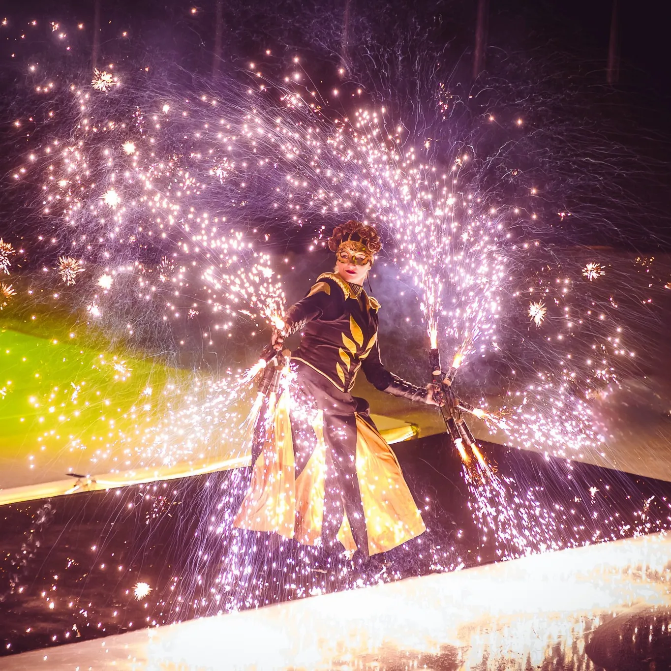 A performer raised above the stage with spark fountains in each hand