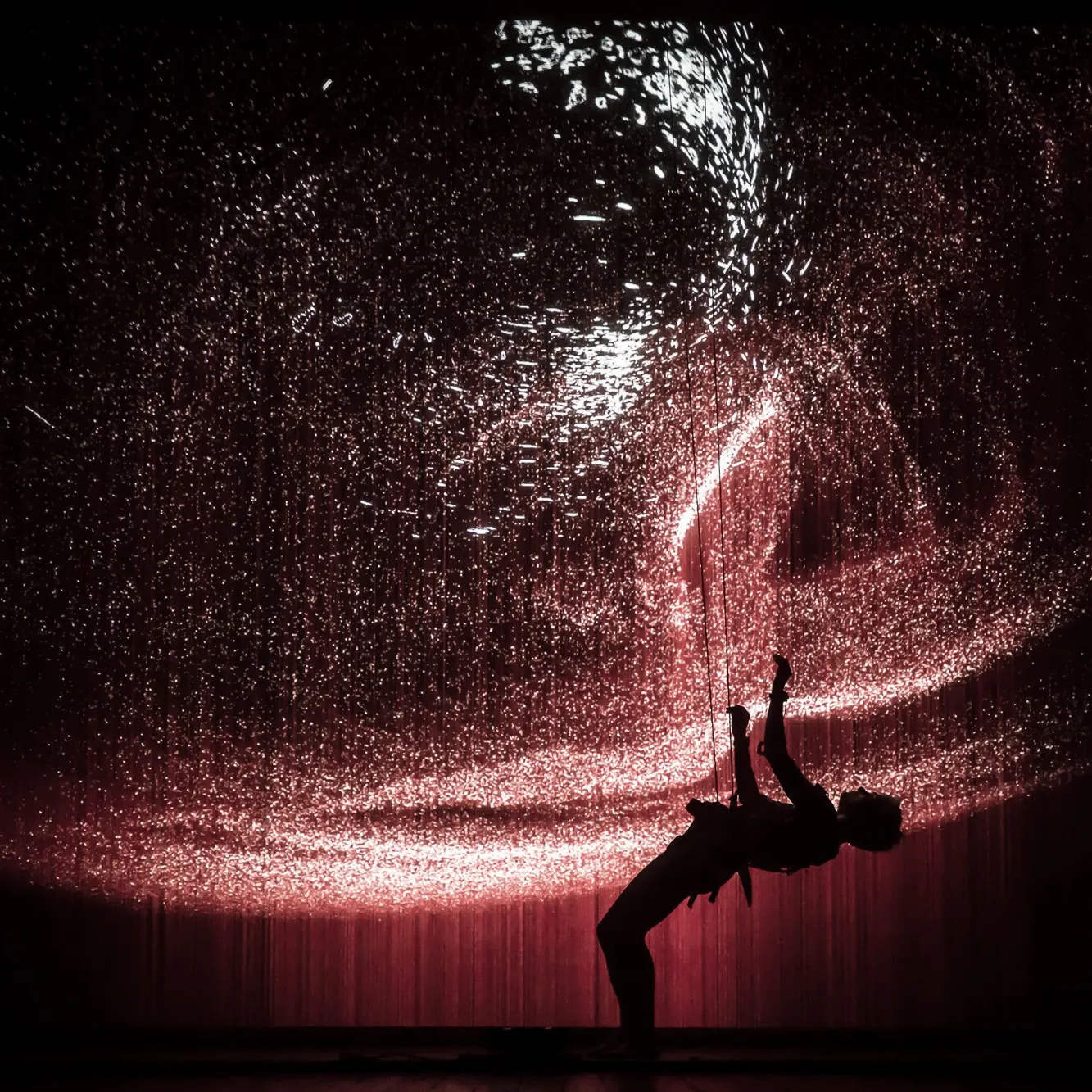 Performer suspended on ropes against a red interactive projection backdrop