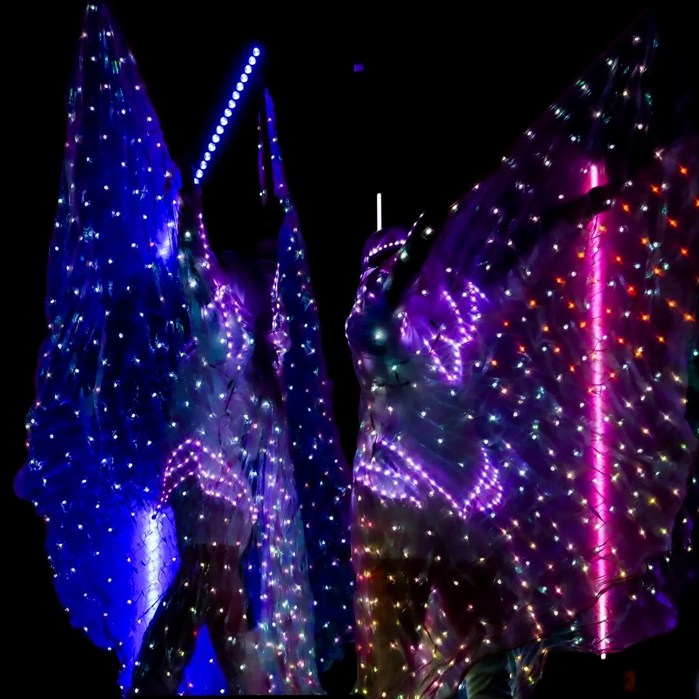 A close-up of LED wings glowing in blue and pink light