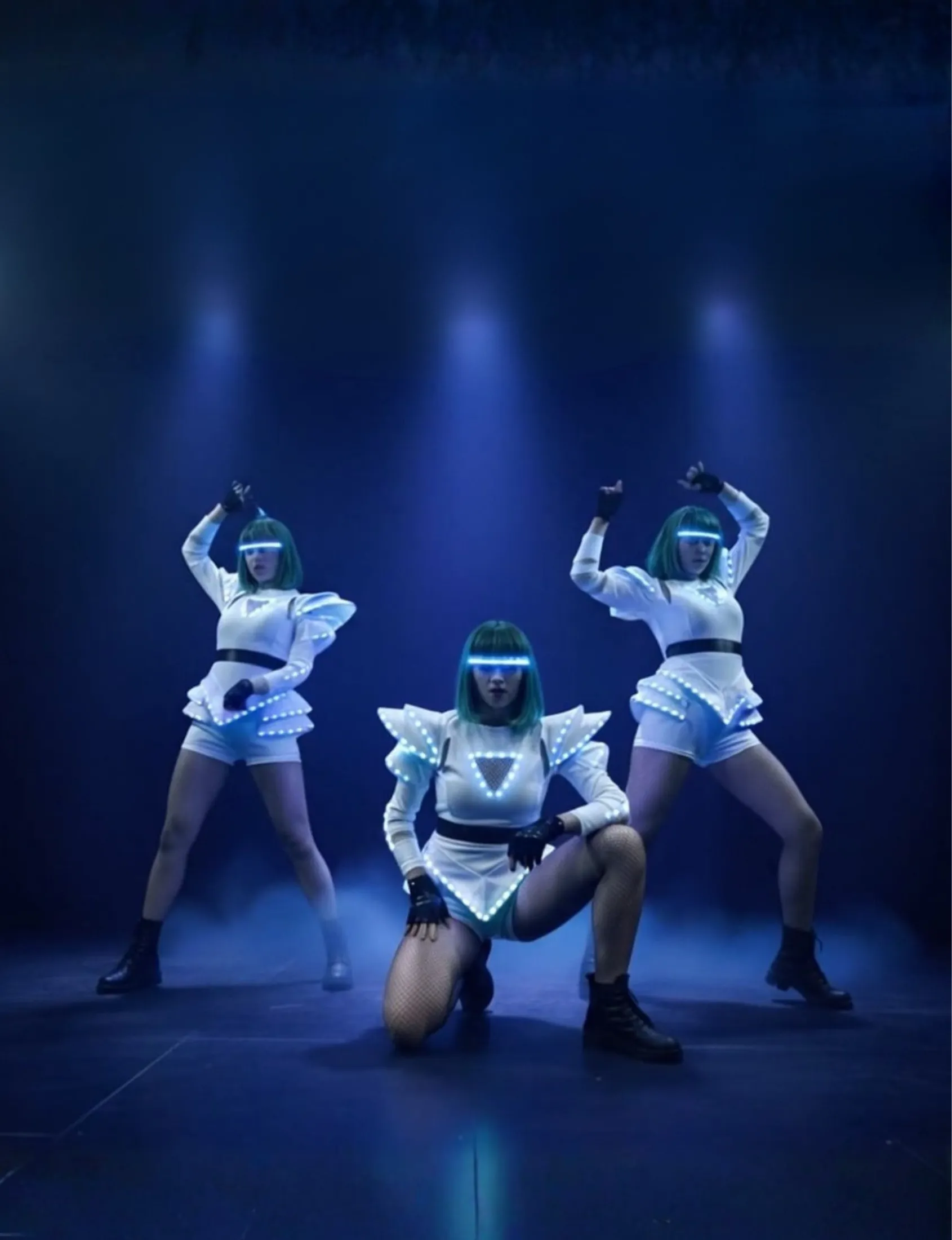 Three dancers in LED costumes perform choreography on stage