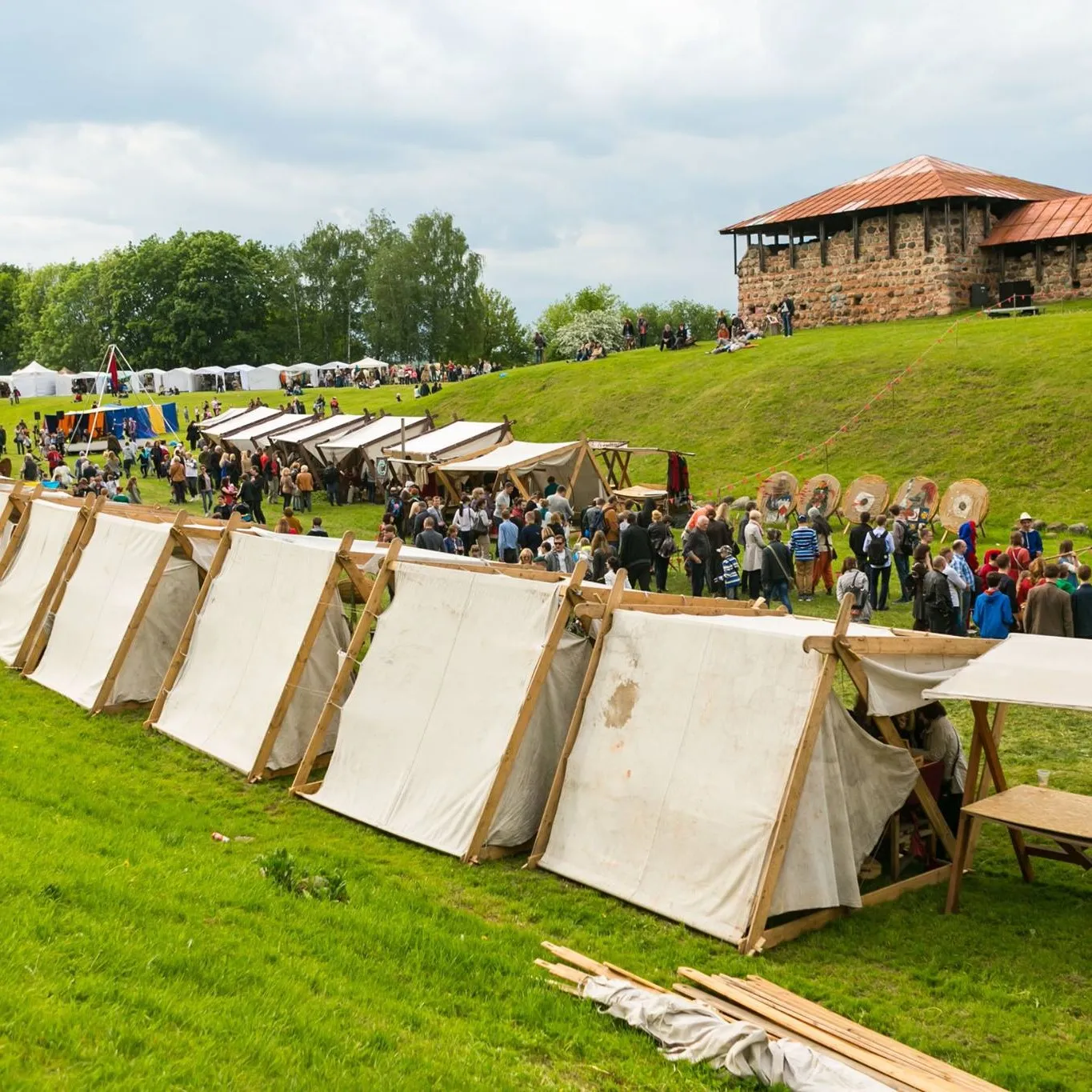 A row of white medieval tents at an outdoor event with archery targets