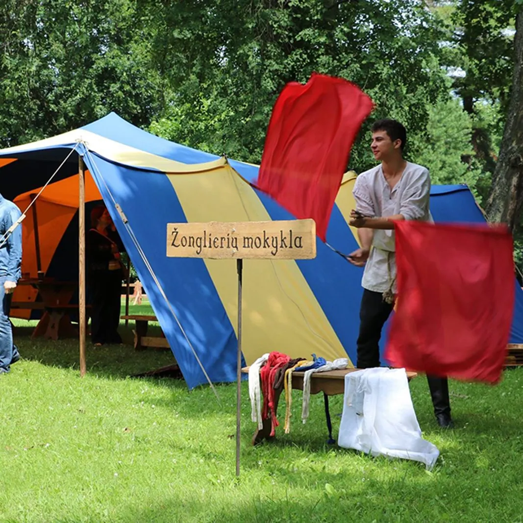 A teenage boy juggles red flags near the juggling school tent