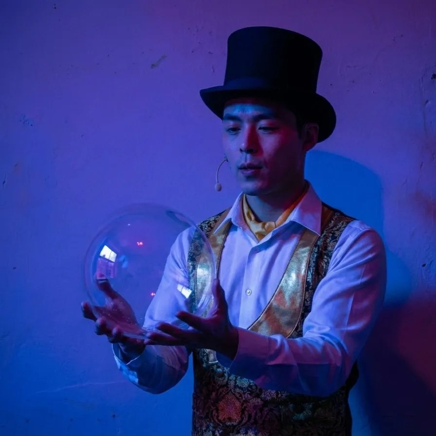A bubble illusionist in a top hat holds a clear bubble in his hands