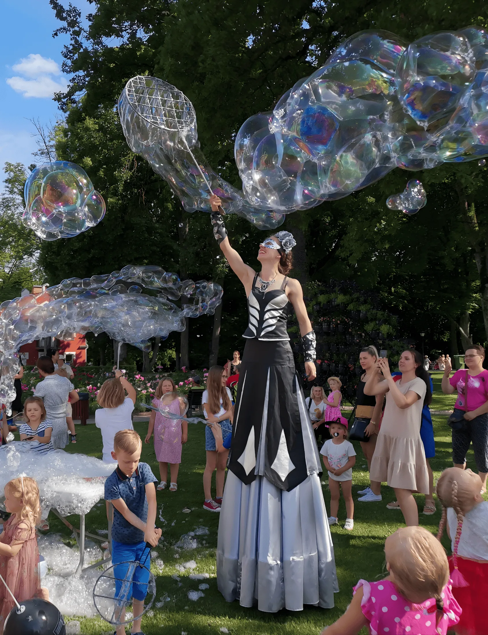 A stilt performer creates giant soap bubbles in the park for onlookers
