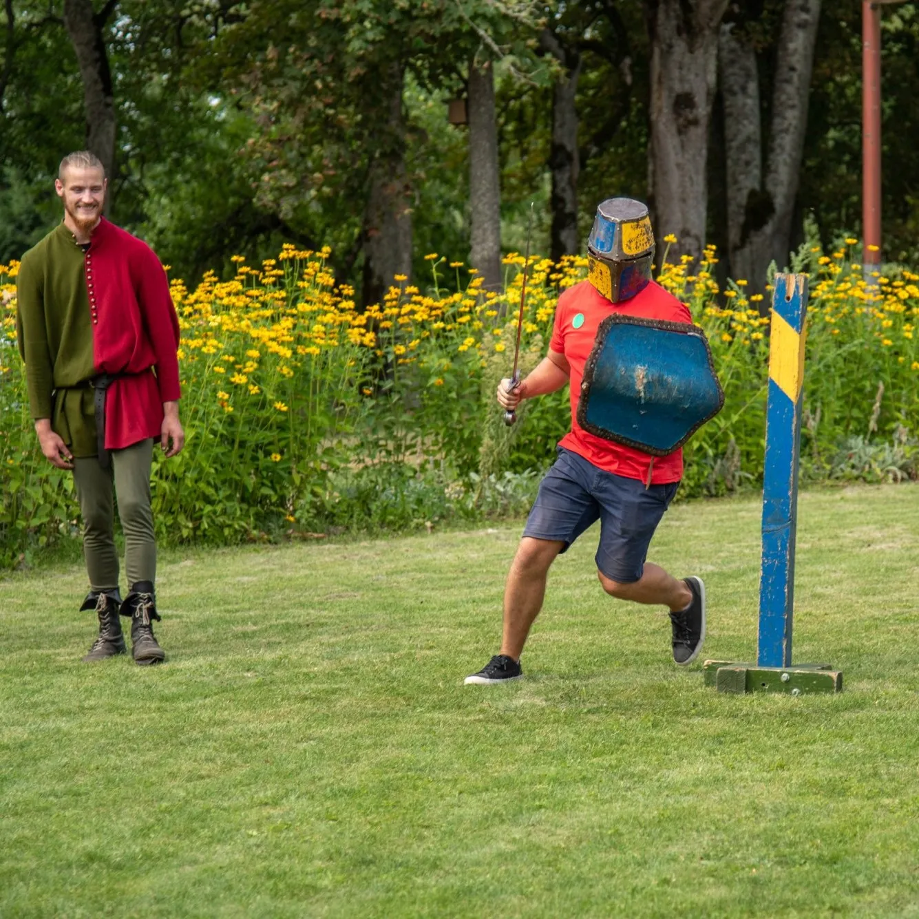 A participant in helmet and shield charges a target in a park setting