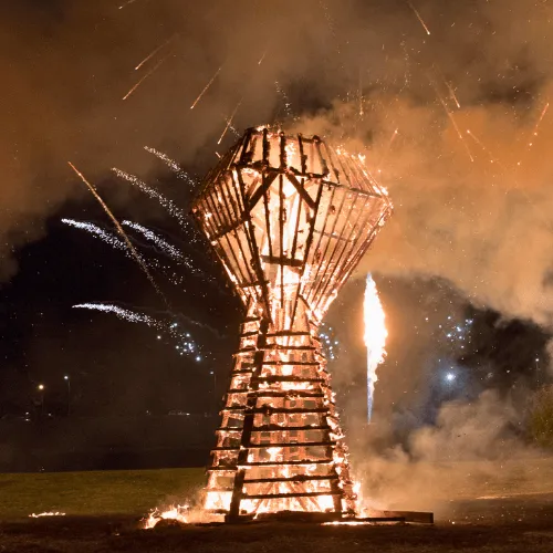 A couple kisses in front of a burning heart-shaped fire sculpture