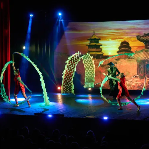 Two performers weave green and red Chinese dragon props through a full stage show