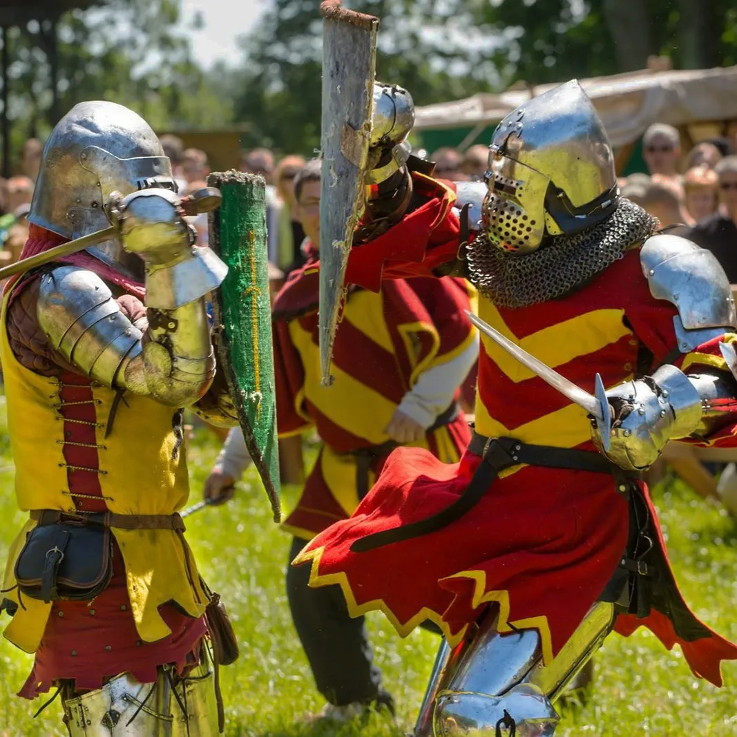 Two knights in yellow and red garb clash swords on the grass