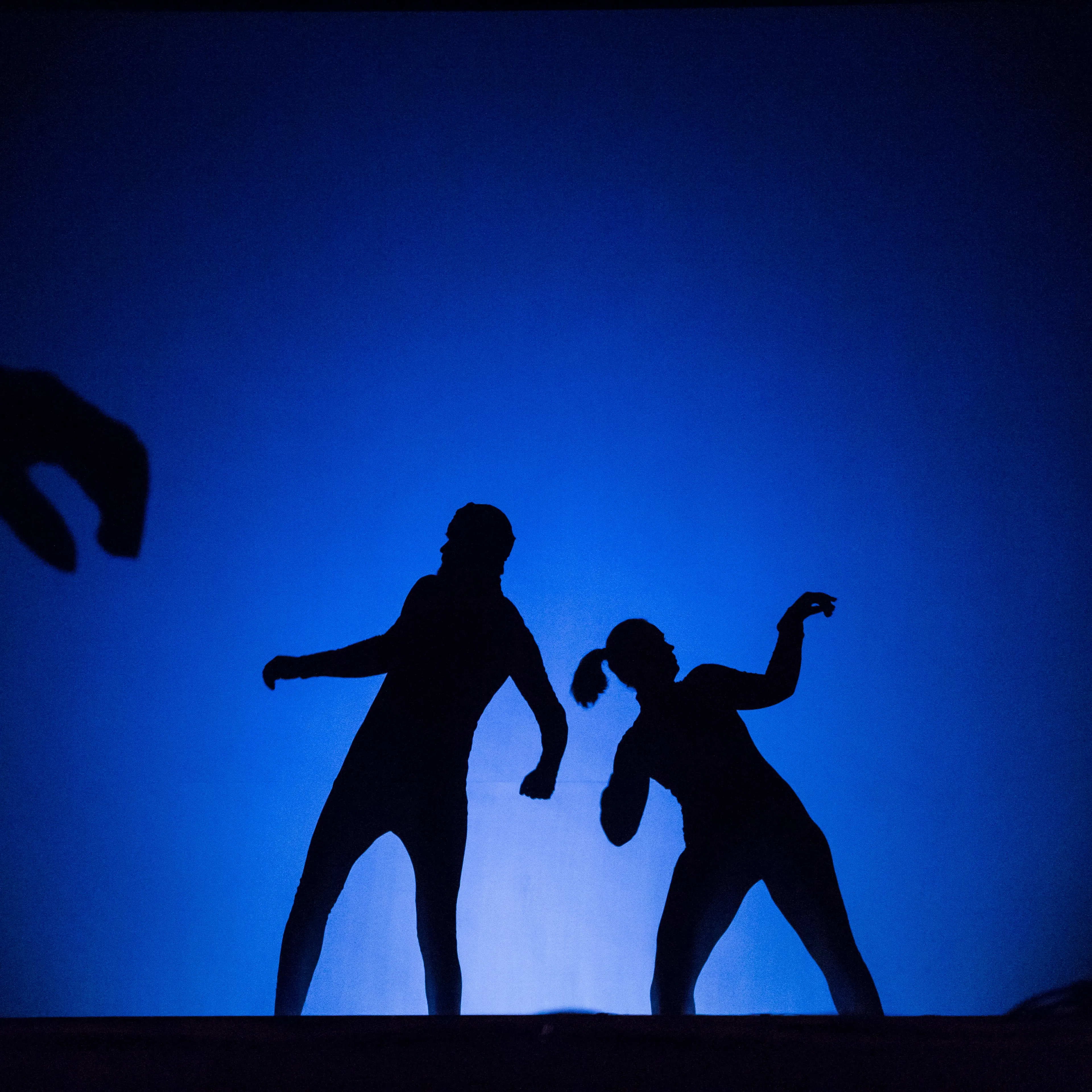 Two silhouettes in a dynamic pose against a blue shadow-theatre backdrop