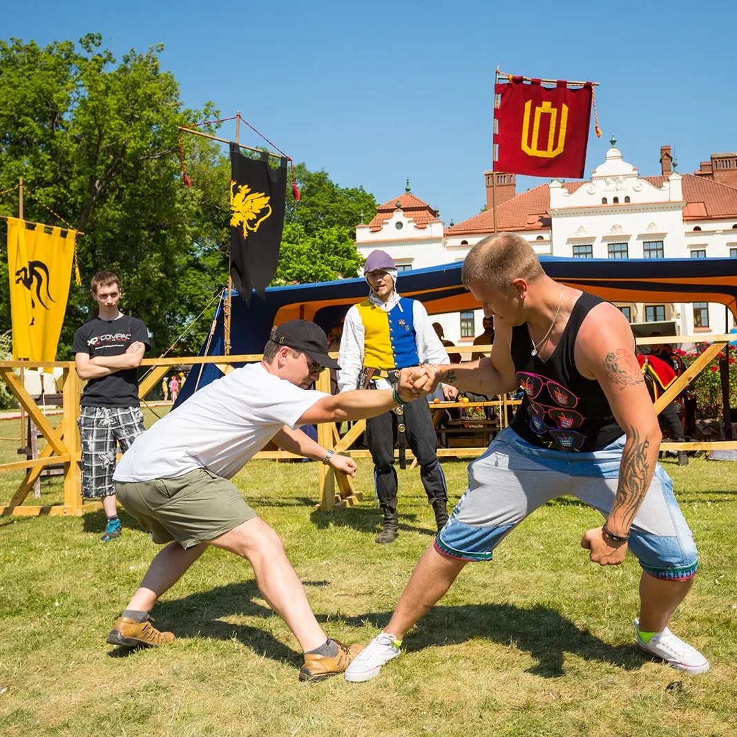 Two men compete in a strength challenge beside flags at an outdoor event
