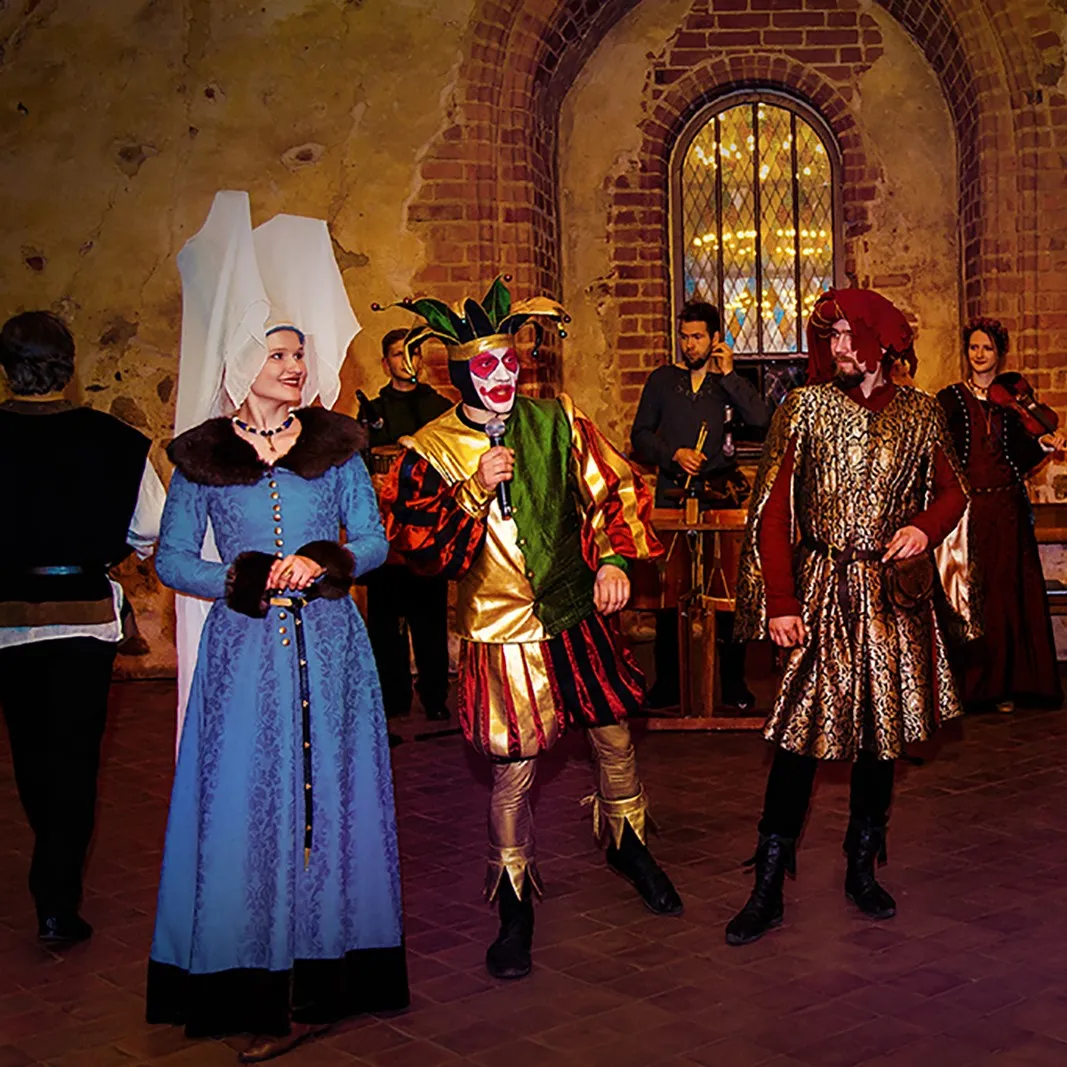 Four courtiers in period banquet costumes in a historic hall