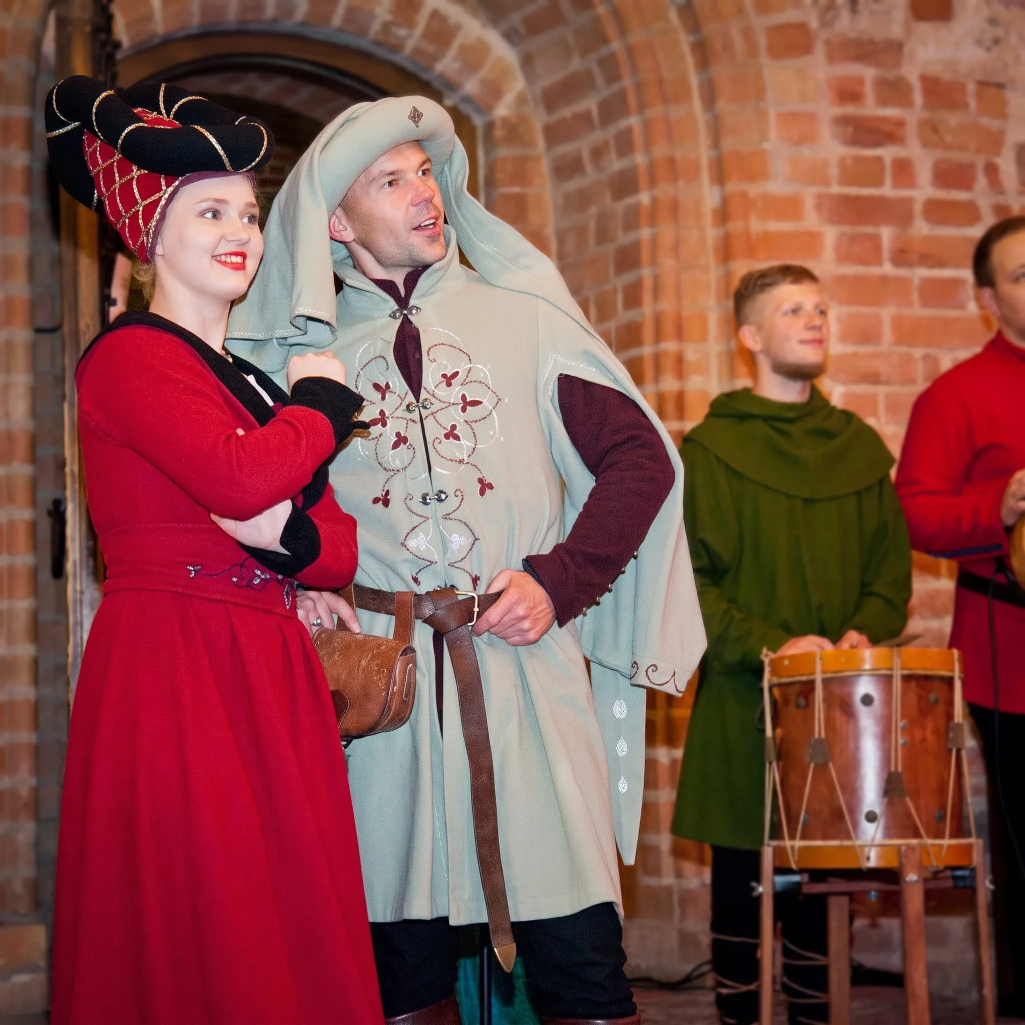 Costumed courtiers and a musician with a drum in a vaulted hall
