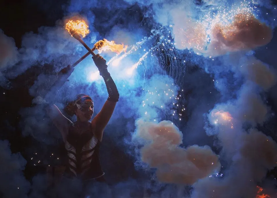 Fire performer raising a burning torch against blue smoke