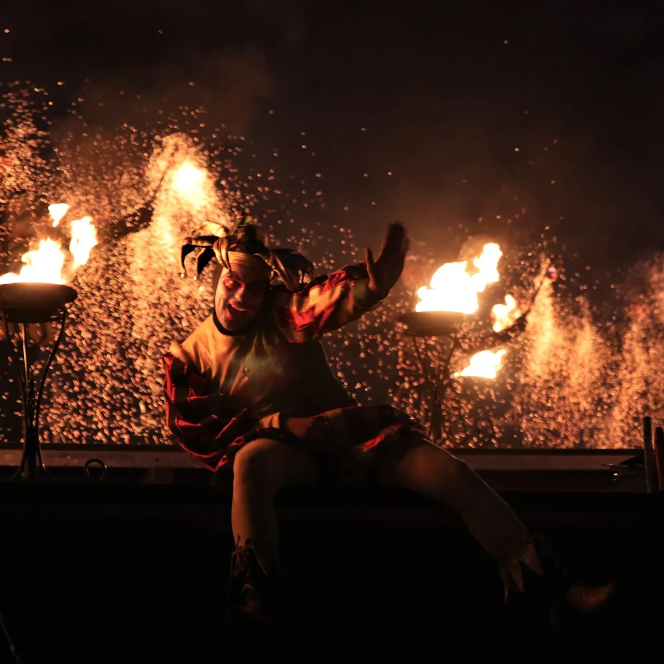 A jester character leaps beside burning torches during the show
