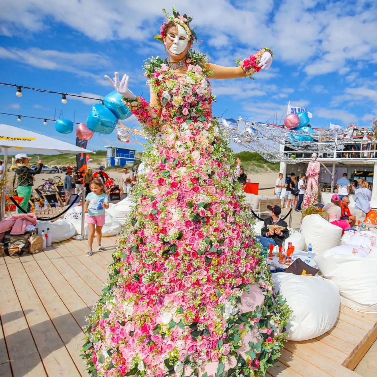 Flower character on stilts in a pink floral gown posing at a beach party