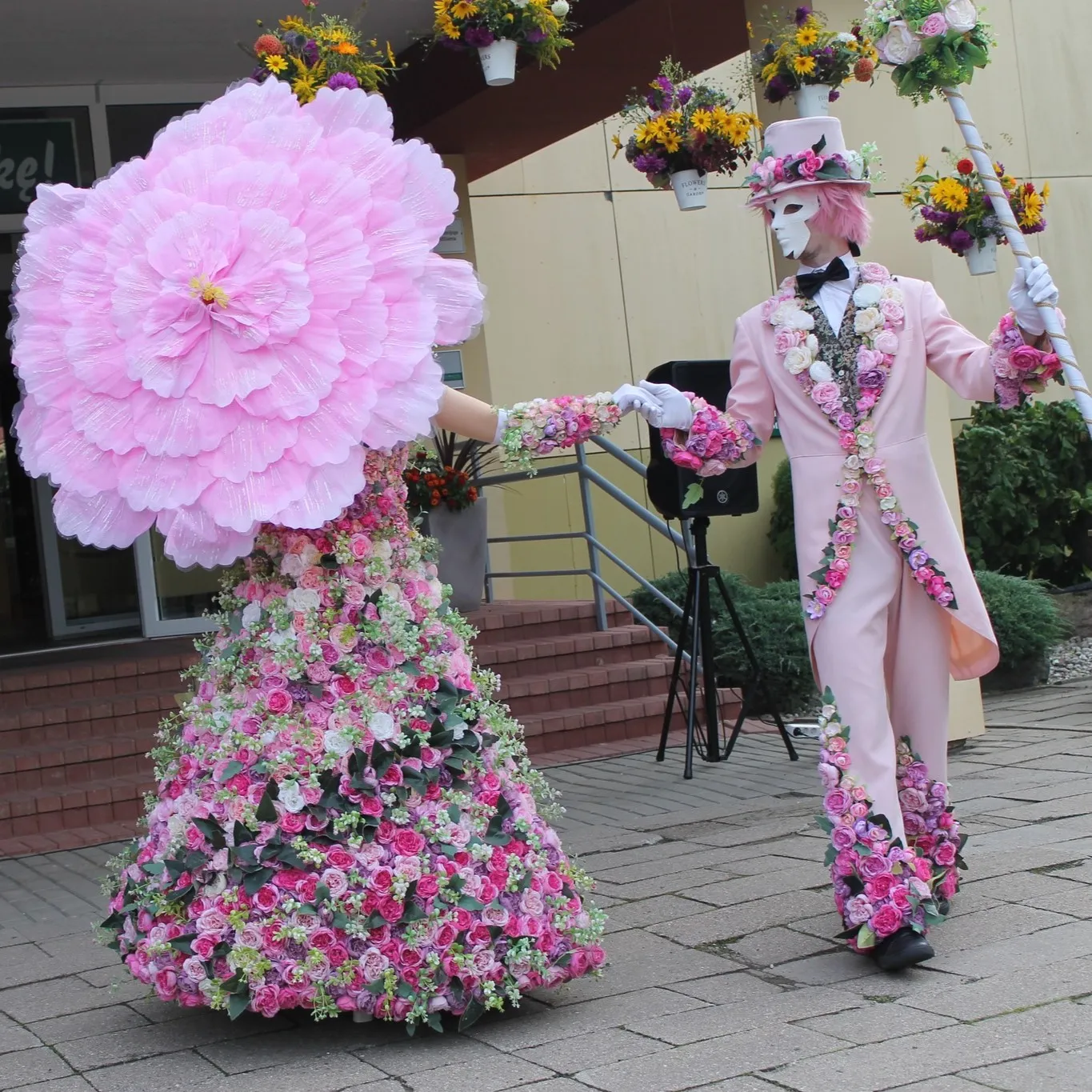 Flower character with a giant pink flower-shaped headpiece near a building entrance