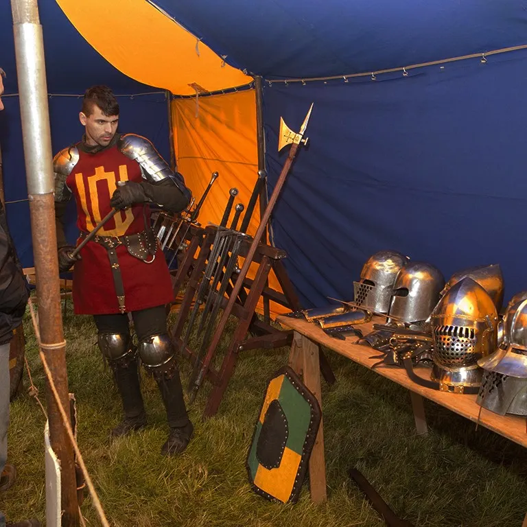A costumed guide arranges weapons and helmets inside the tent