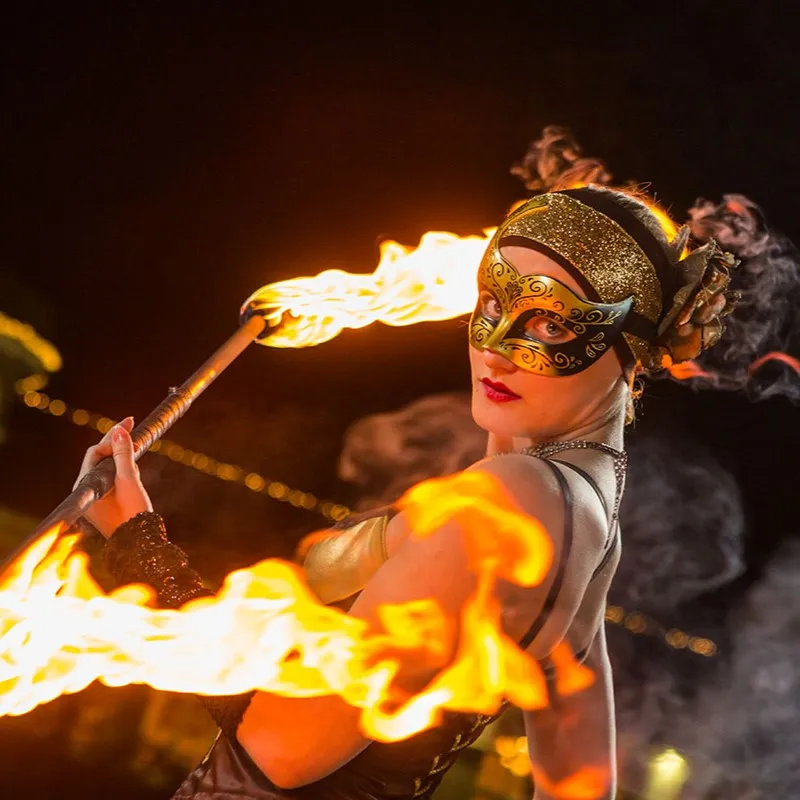 A performer in a golden mask poses with a blazing tool