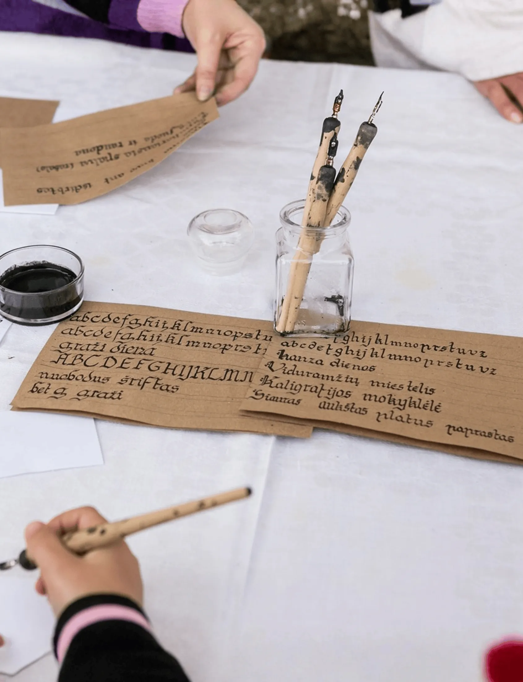A calligraphy workshop table with quills, ink and a medieval alphabet on paper