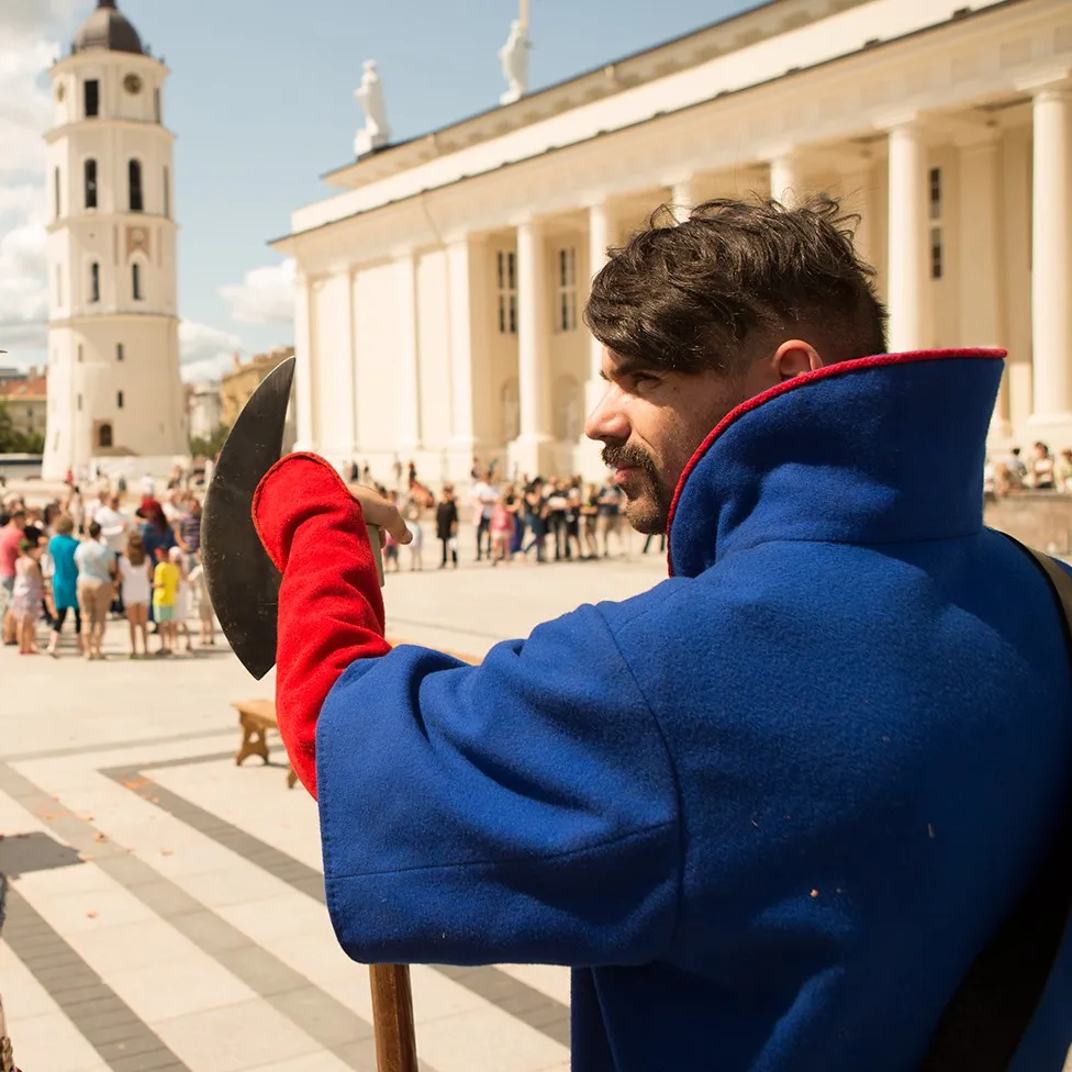 A warrior with a halberd stands in a city square near the cathedral belfry