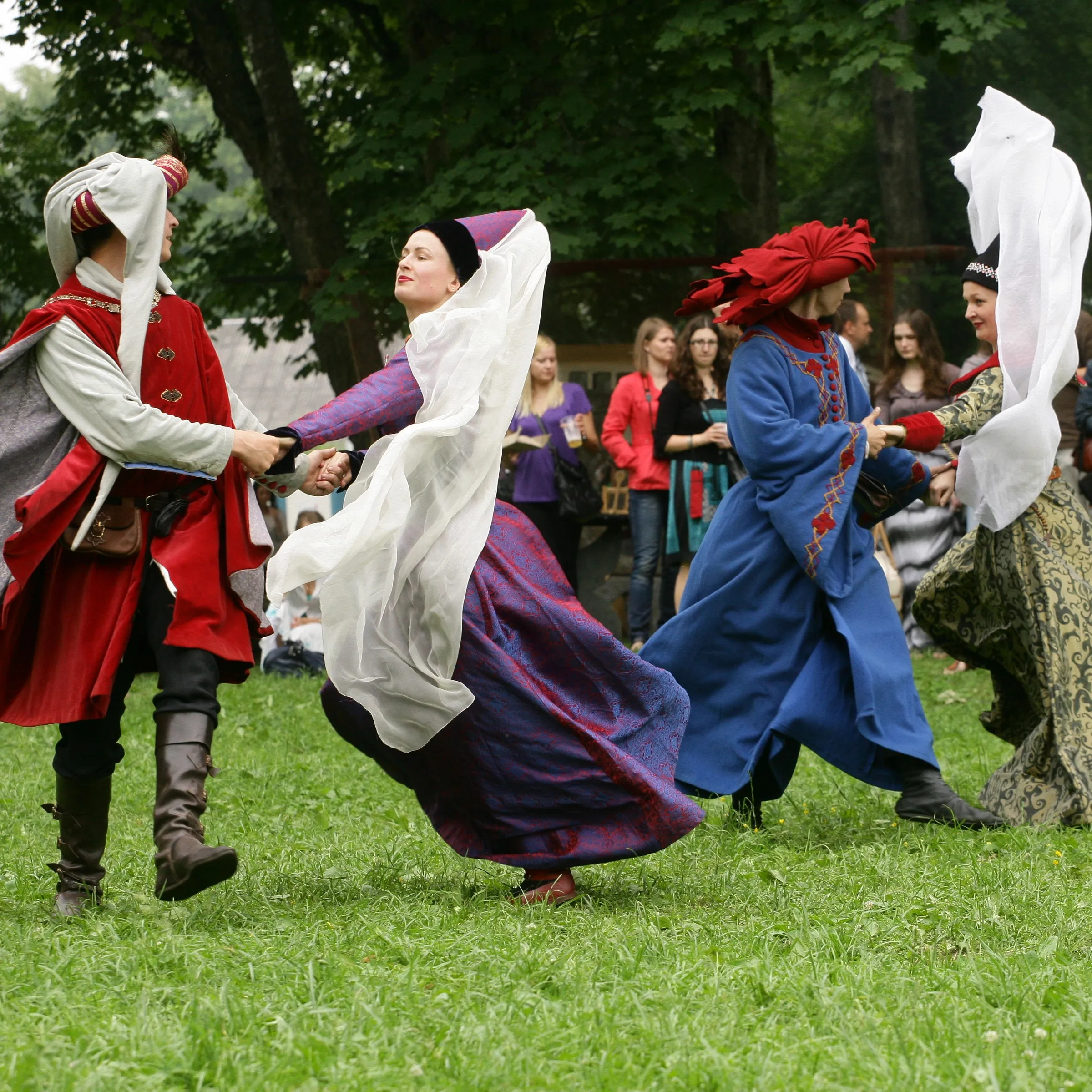 Four dancers in medieval costume spin in a circle dance in the park