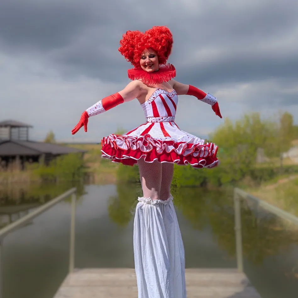 A stilt-walking character in a red-and-white circus doll dress