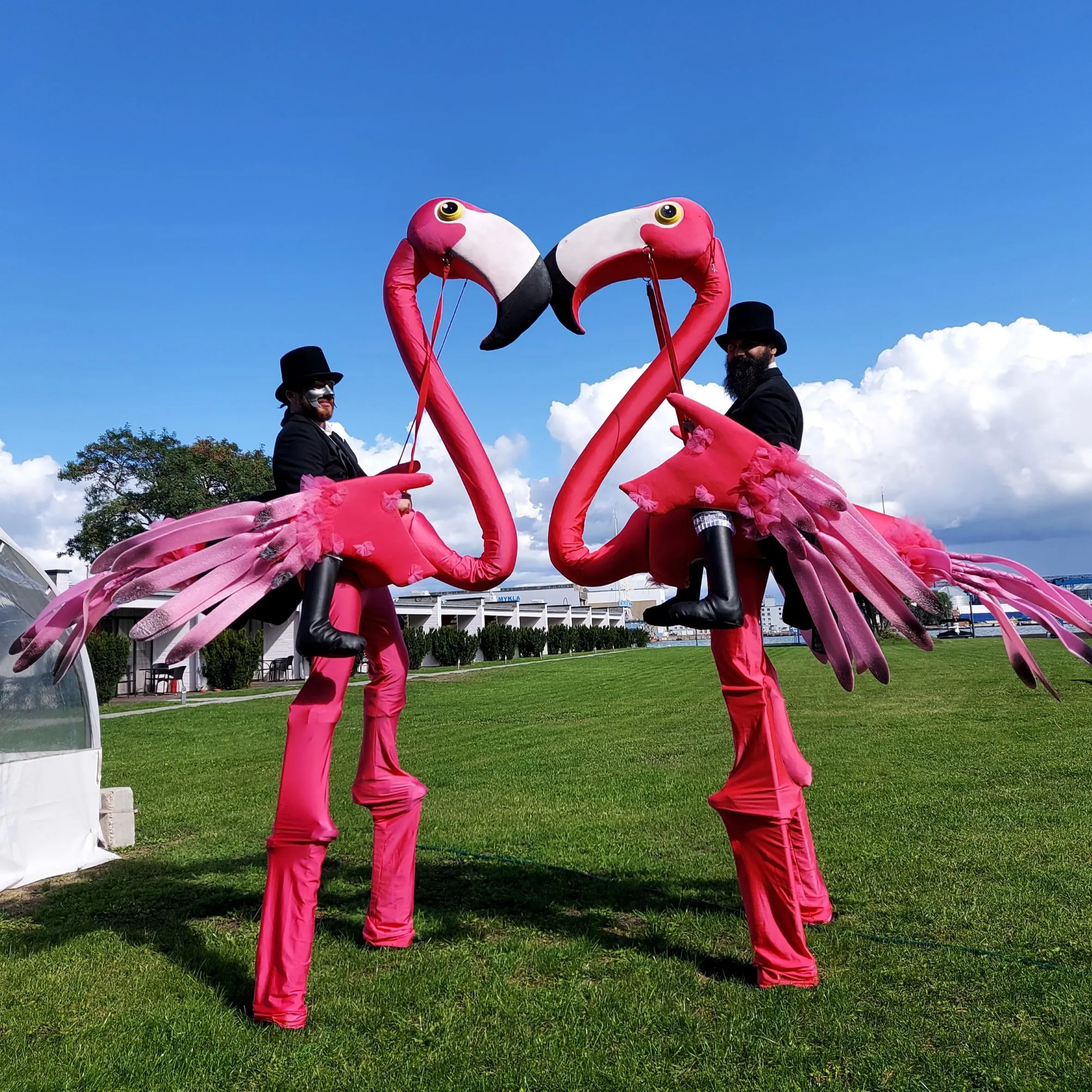 Two stilt-walking flamingo characters form a heart with their necks