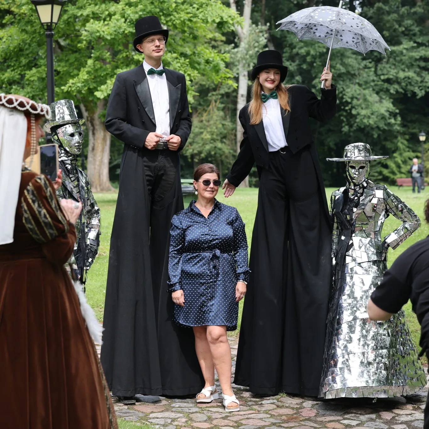 Stilt walkers pose for a photo with a guest in the park