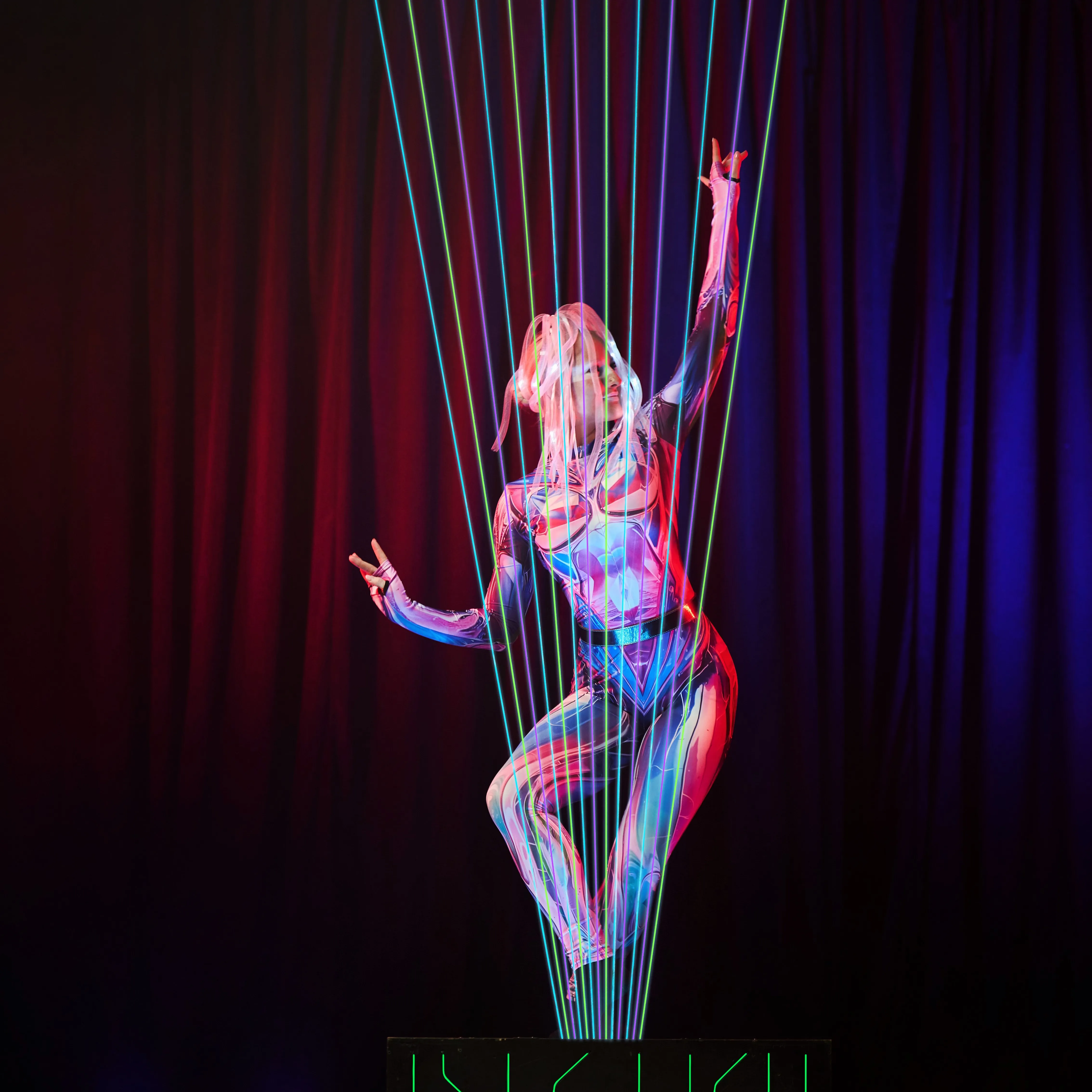 The performer raises their arms on a lit platform amid laser beams