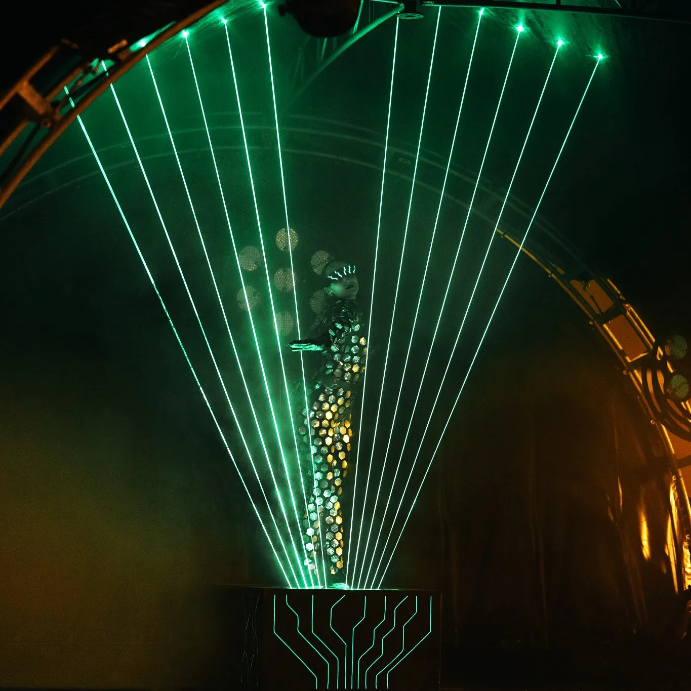 The performer stands inside a large volumetric green laser pyramid