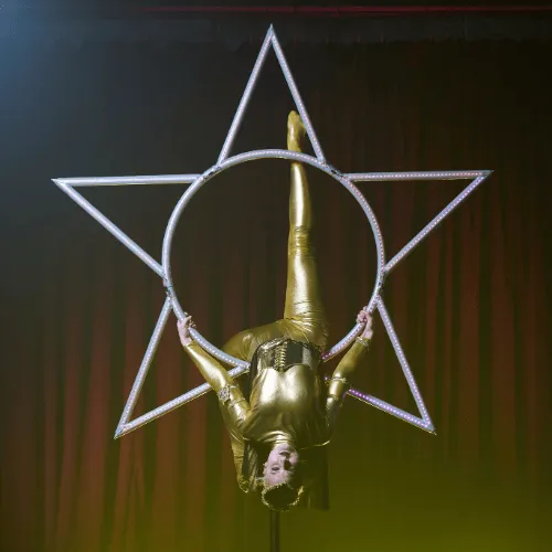 An acrobat upside down with an extended leg inside the glowing Star apparatus