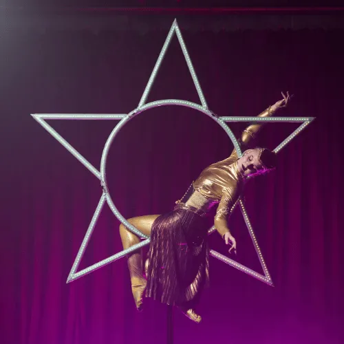 An acrobat leaning back inside the glowing Star apparatus under pink stage light