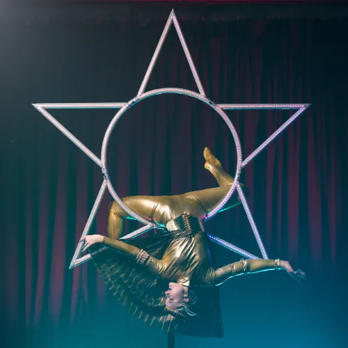 An acrobat in a flexible pose inside a glowing golden Star apparatus