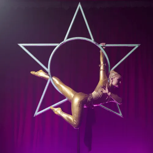 An acrobat in a golden costume inside the Star apparatus against a purple stage light