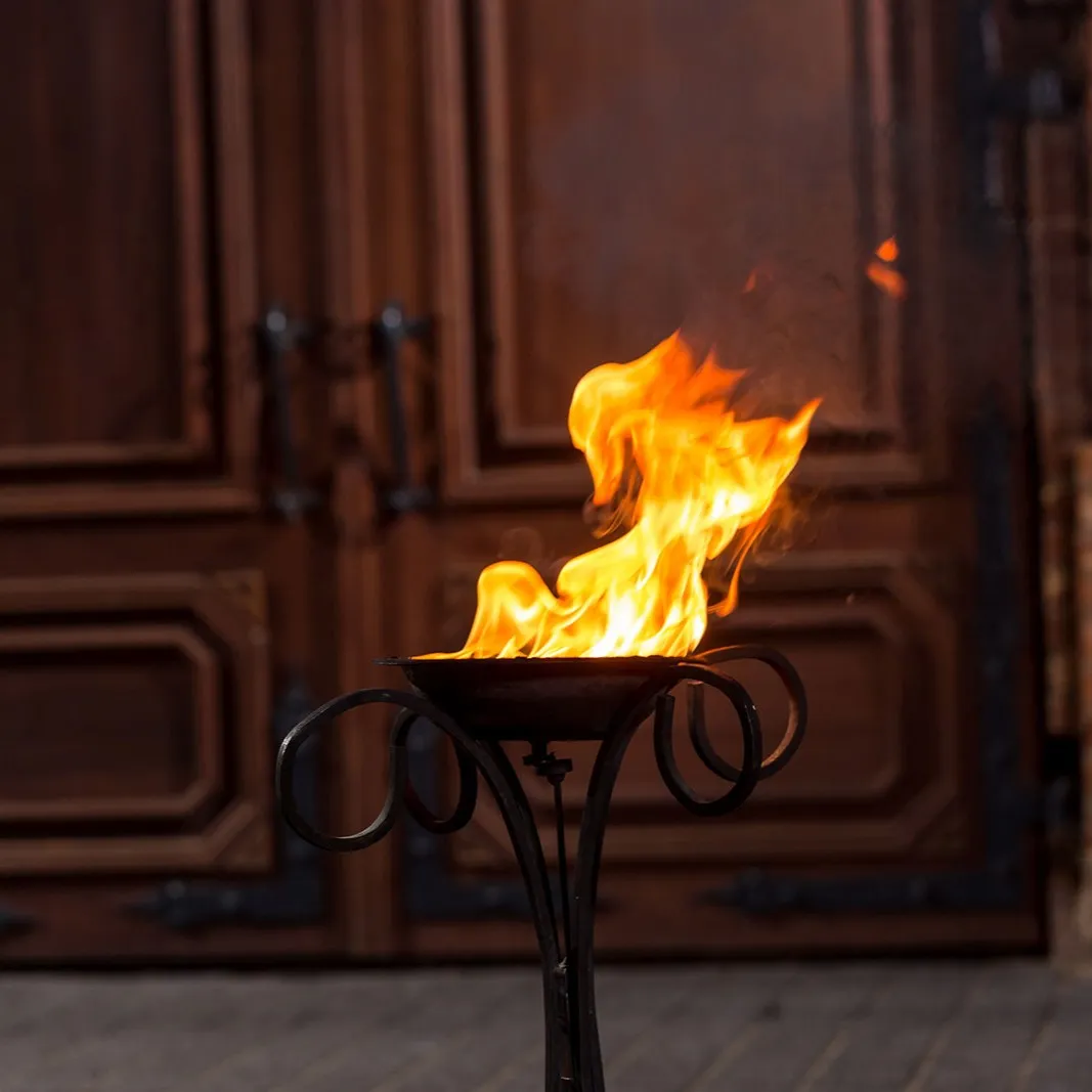 A tall flame burns on a single fire stand beside a wooden door