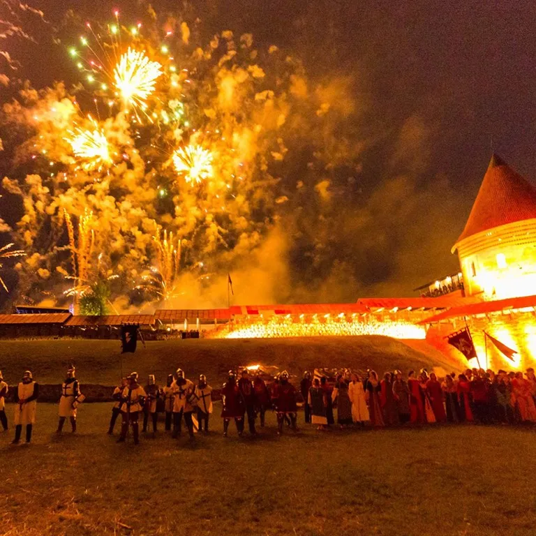 Fireworks above a lit-up castle in front of a line of assembled knights