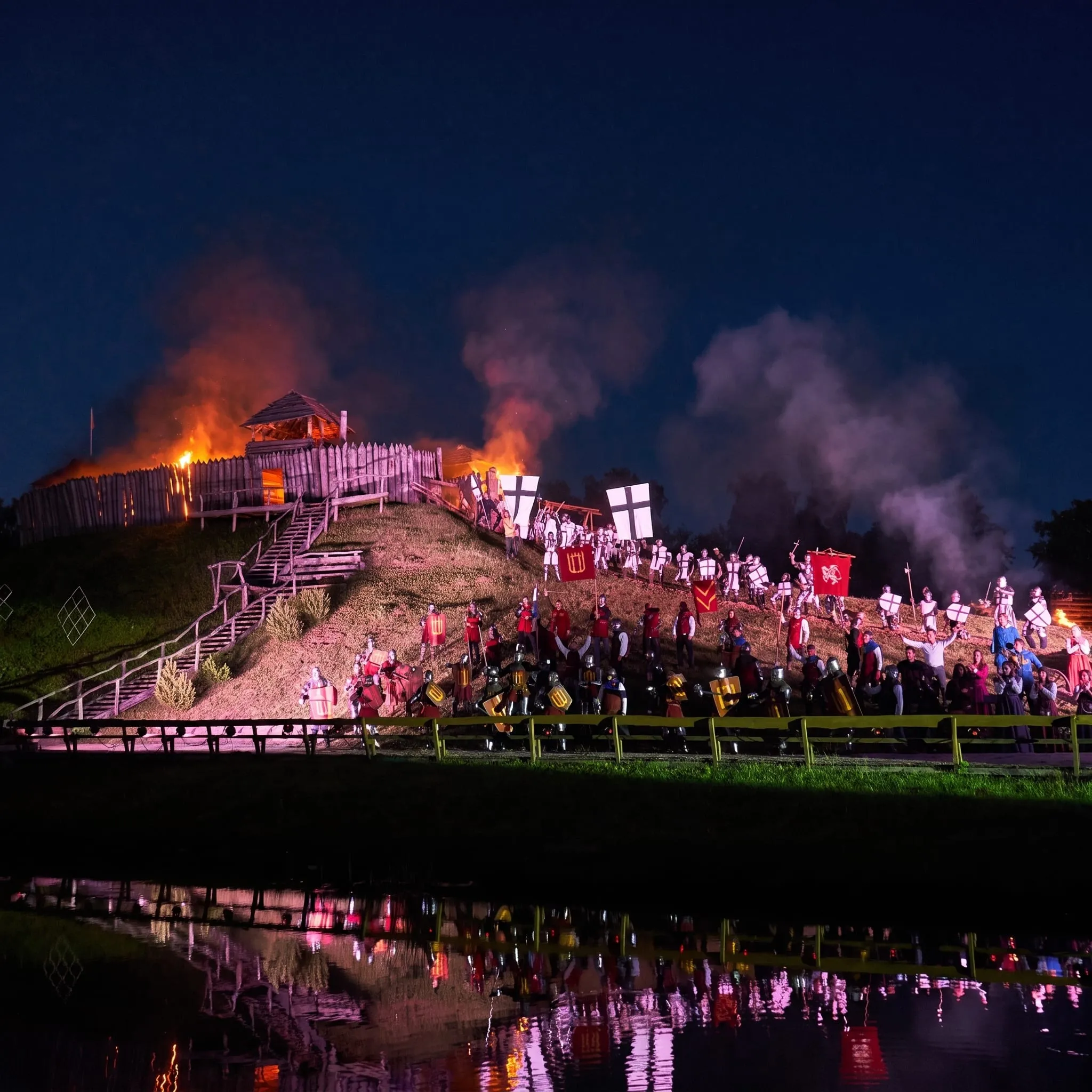 A night scene with a burning wooden fortress and knights holding banners