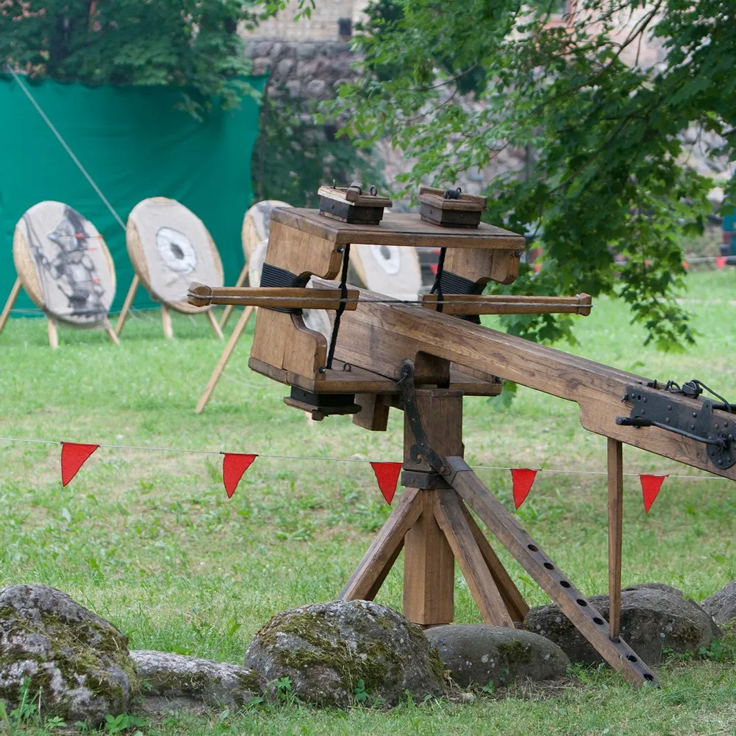 A large wooden siege crossbow device in a castle courtyard near targets