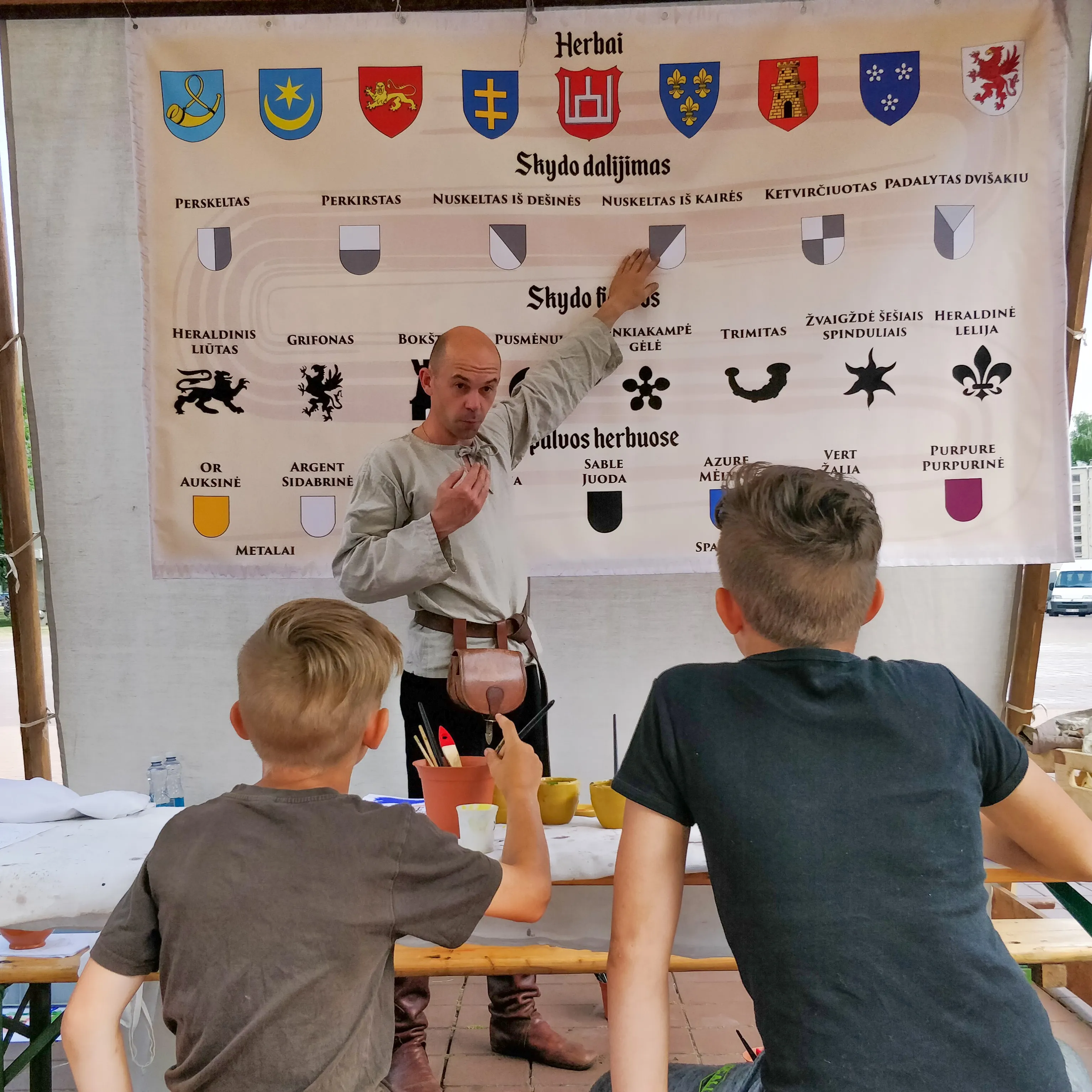 A craftsman explains heraldic symbols and shield divisions to children