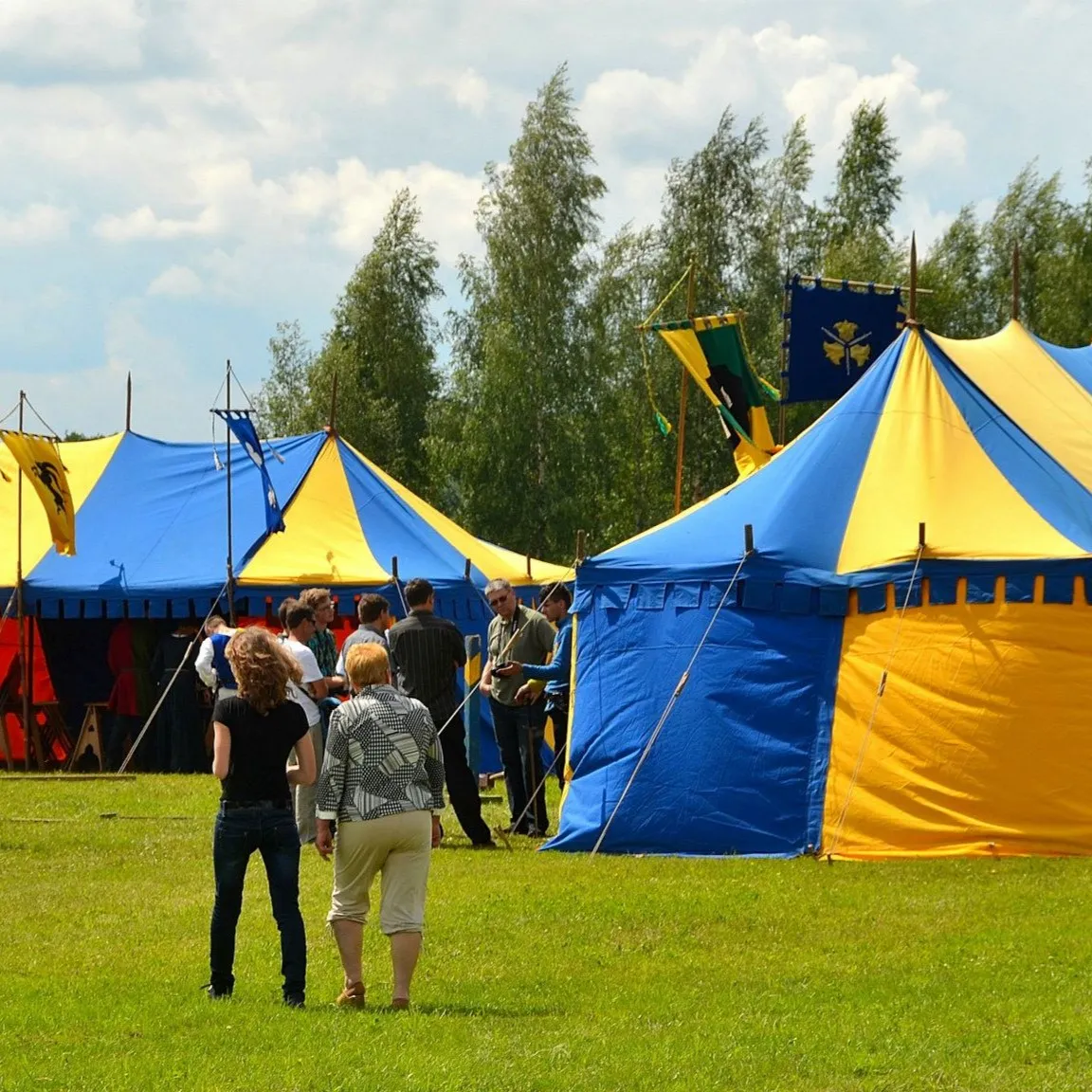 Blue and yellow tents on a lawn with event guests nearby