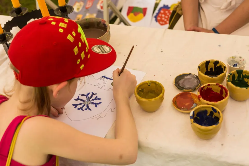Girl painting a medieval ornament with a brush beside bowls of pigment