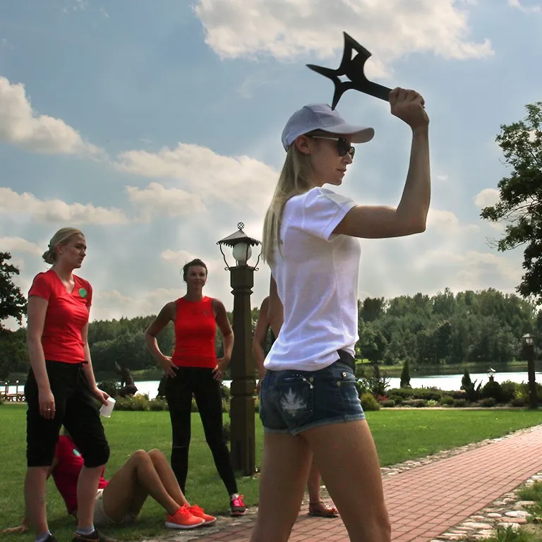 A woman in a cap prepares to throw an axe in a lakeside park
