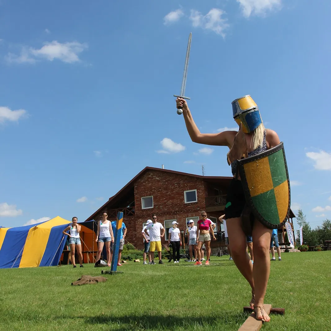 A woman with a helmet, shield and sword poses on a green lawn